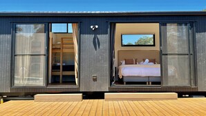 A modern cabin with a large sliding glass door leading to a bedroom with a bed and a small window. - Lovedale Abode 13 bedrooms with heated pool & Acres (Lovedale)