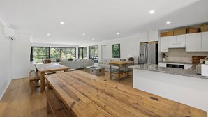 A modern kitchen with white cabinets, a wooden dining table, and a built-in island with a sink. - Lovedale Abode 13 bedrooms with heated pool & Acres (Lovedale)