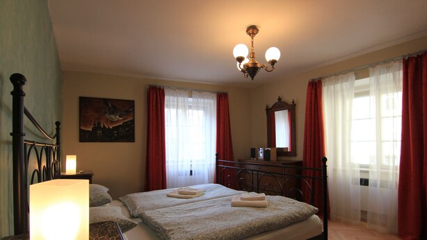 Een hotelkamer met een bed, nachtkastje, lamp, schilderij en een kroonluchter.
