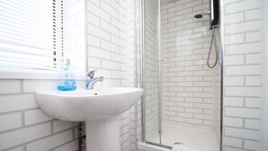 A bathroom with a white sink, a glass shower enclosure, and a window with blinds. - Cozy Studio Retreat in Swansea (SWANSEA)
