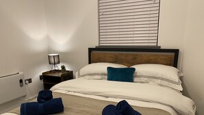 Una camera d'albergo con un letto, un comodino, una lampada e una finestra con persiane.