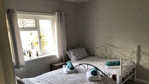 Ein Schlafzimmer mit einem Einzelbett, einem Nachttisch und einem Fenster mit Vorhängen.