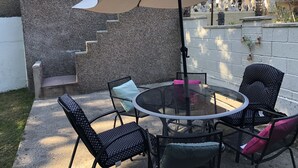 Eine Terrasse mit einem runden Tisch, Stühlen, einem großen Sonnenschirm und einer Steinmauer.