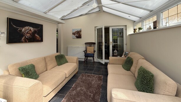 Ein Wintergarten mit zwei beigen Sofas, grünen Kissen und Bildern an den Wänden.