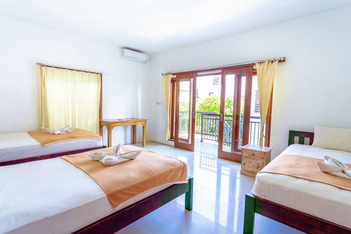A hotel room with two beds, a small table, and a view of the outside.