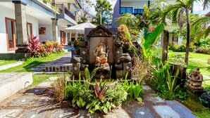 A courtyard with a statue, lush greenery, and a building with a red roof. - D'Canggu Homestay (Canggu)