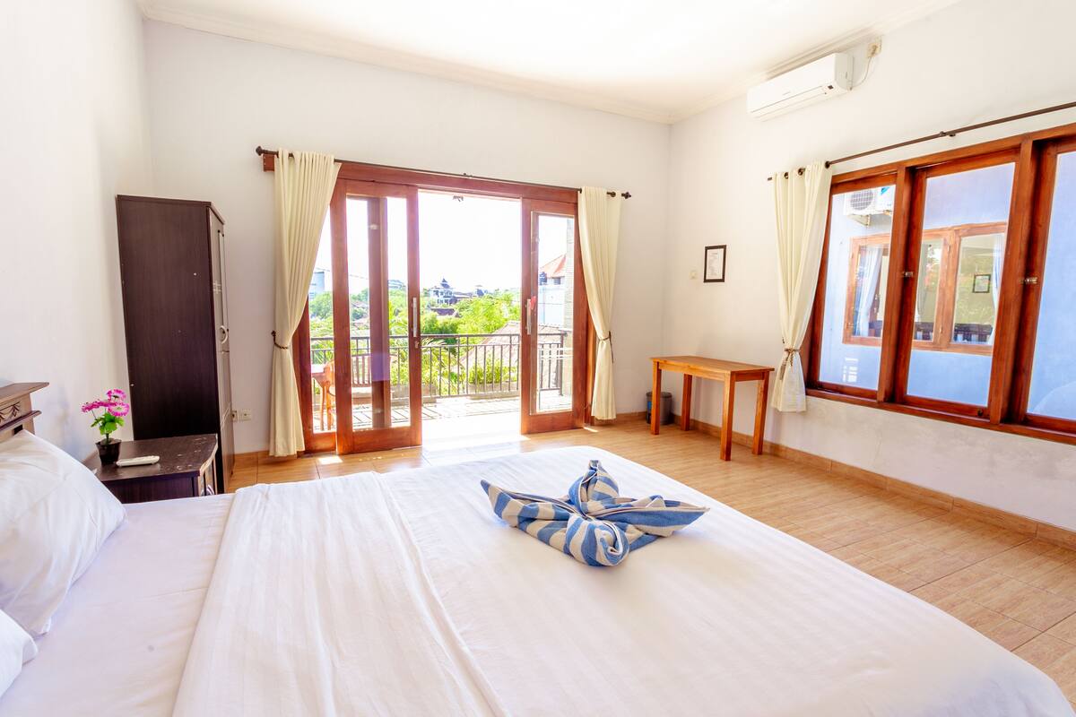 A hotel room with a bed, a desk, a wardrobe, and a balcony with a view.