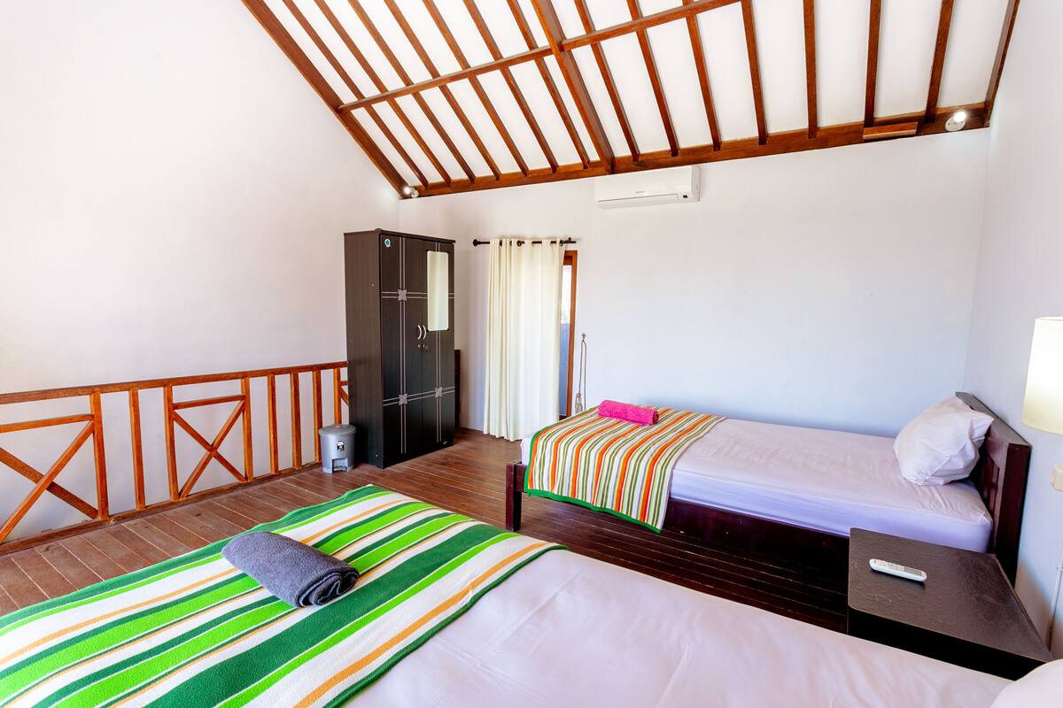 A hotel room with two beds, a wardrobe, a small table, and a ceiling fan.