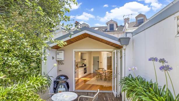 A patio with a table and chairs, a motorcycle, and a view into a house with a kitchen and dining area. - Family home in the heart of Paddington (Paddington)