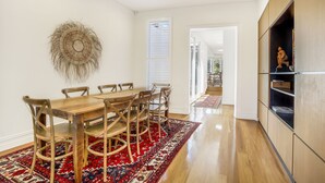 A dining area with a wooden table and chairs, a red patterned rug, and a wall-mounted decorative piece. - Family home in the heart of Paddington (Paddington)