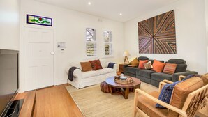 A living room with a white door, two windows with shutters, a large abstract painting, a white sofa, a grey sofa, and a wooden coffee table. - Family home in the heart of Paddington (Paddington)