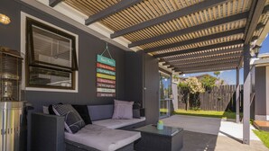 Een overdekt terras met een bank en een bijzettafeltje, een barbecue en een muur met inspirerende borden.