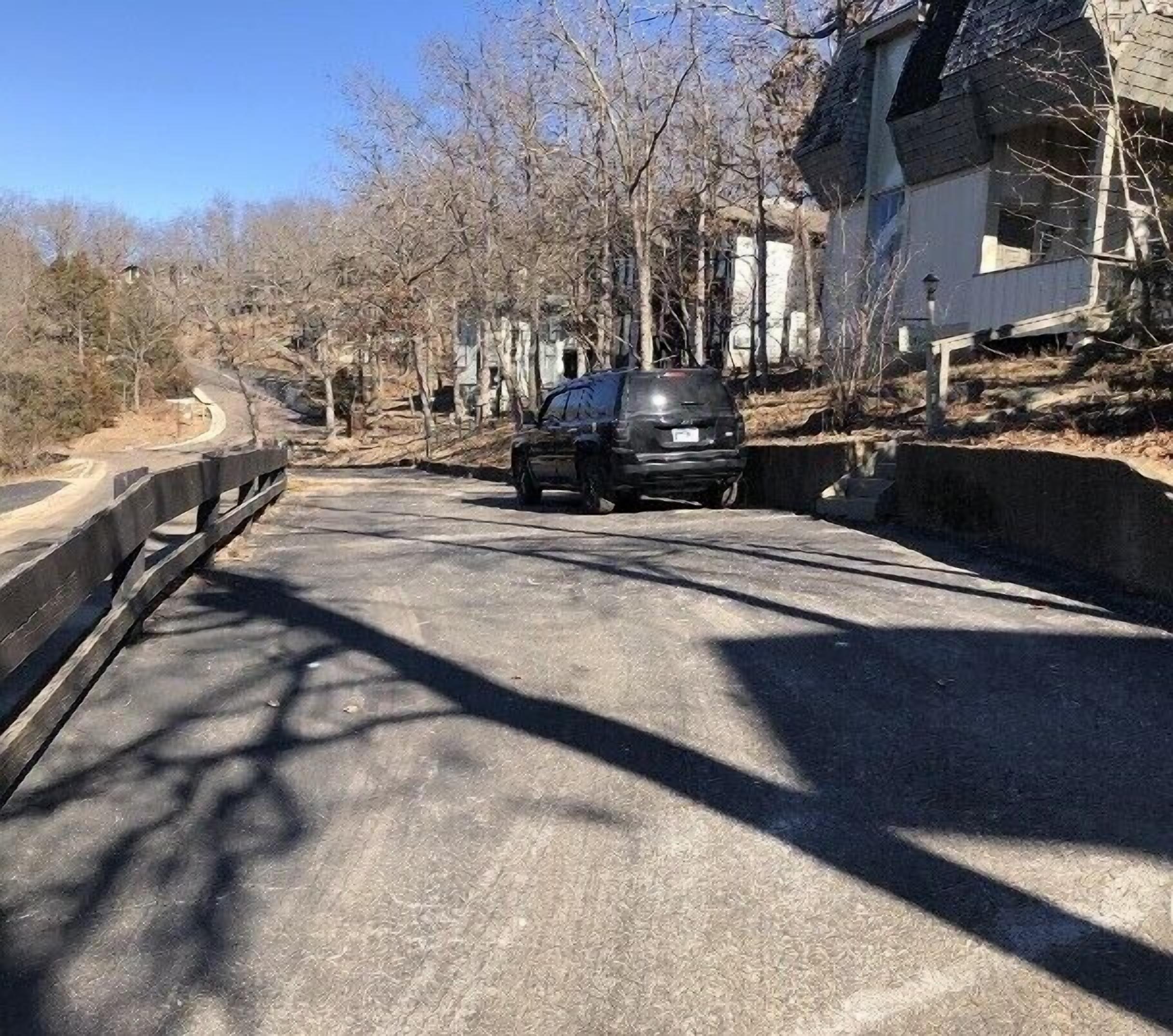 A road with a car parked on the side, surrounded by trees and buildings.