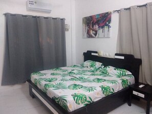 A bedroom with a bed, a nightstand, a wall-mounted air conditioner, and a painting.
