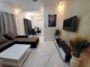 A modern living room with a sofa, coffee table, TV, and a dining area with chairs and a table. - 2 bedrooms - Luxury apartment Mènontin (Cotonou)