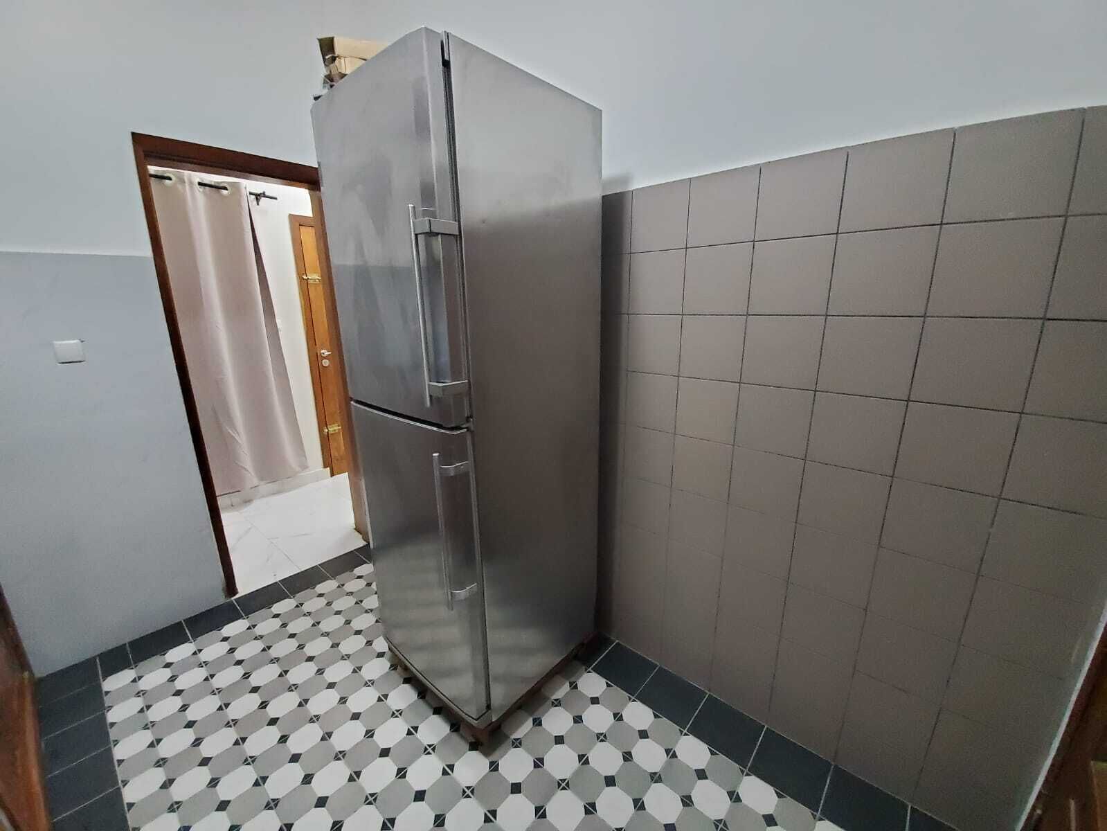 Een keuken met een roestvrijstalen koelkast, betegelde vloer en een houten deur.