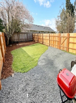 A backyard with a wooden fence, a lawn, and a barbecue grill.