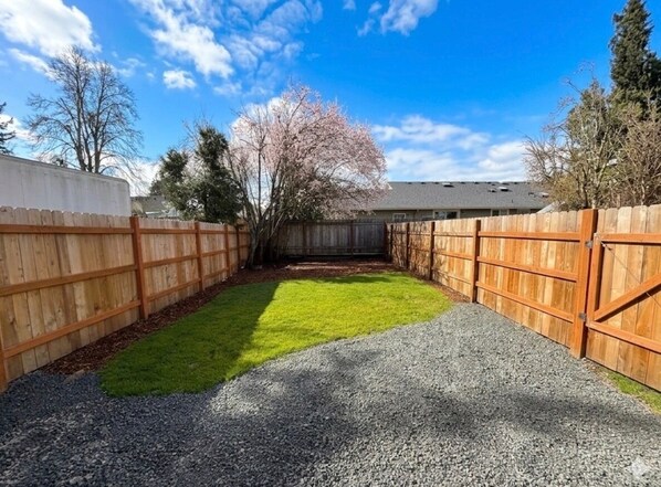 A fenced backyard with a gravel path, a grassy area, and a wooden fence.