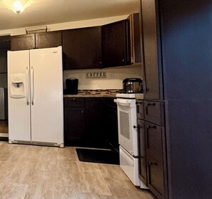 A compact kitchen with a white refrigerator, dark cabinets, a coffee maker, and a stove.