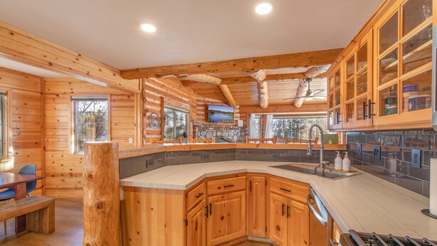 A log cabin interior with a kitchen featuring wooden cabinets, a stone fireplace, and a large island with a sink. - Private tree top cabin, Mountain Views, 5 min to slopes, Walk to zoo & food (Big Bear)