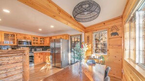 A log cabin interior with wooden walls, a large wooden dining table, and a kitchen with stainless steel appliances. - Private tree top cabin, Mountain Views, 5 min to slopes, Walk to zoo & food (Big Bear)