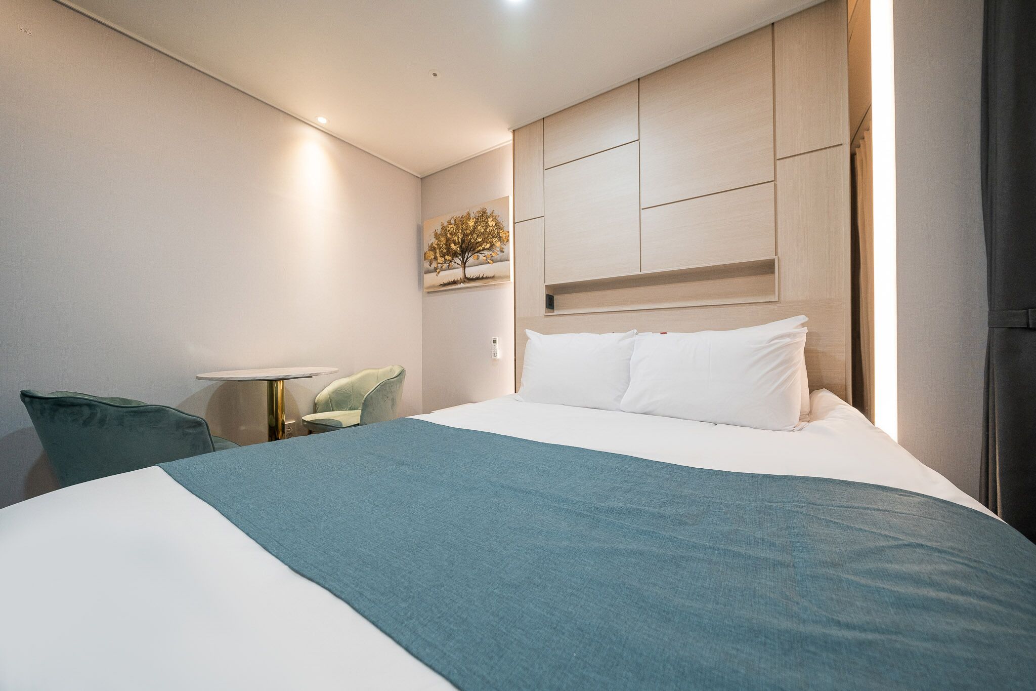 Een moderne hotelkamer met een groot bed, nachtkastje, stoel en een kunstwerk aan de muur.