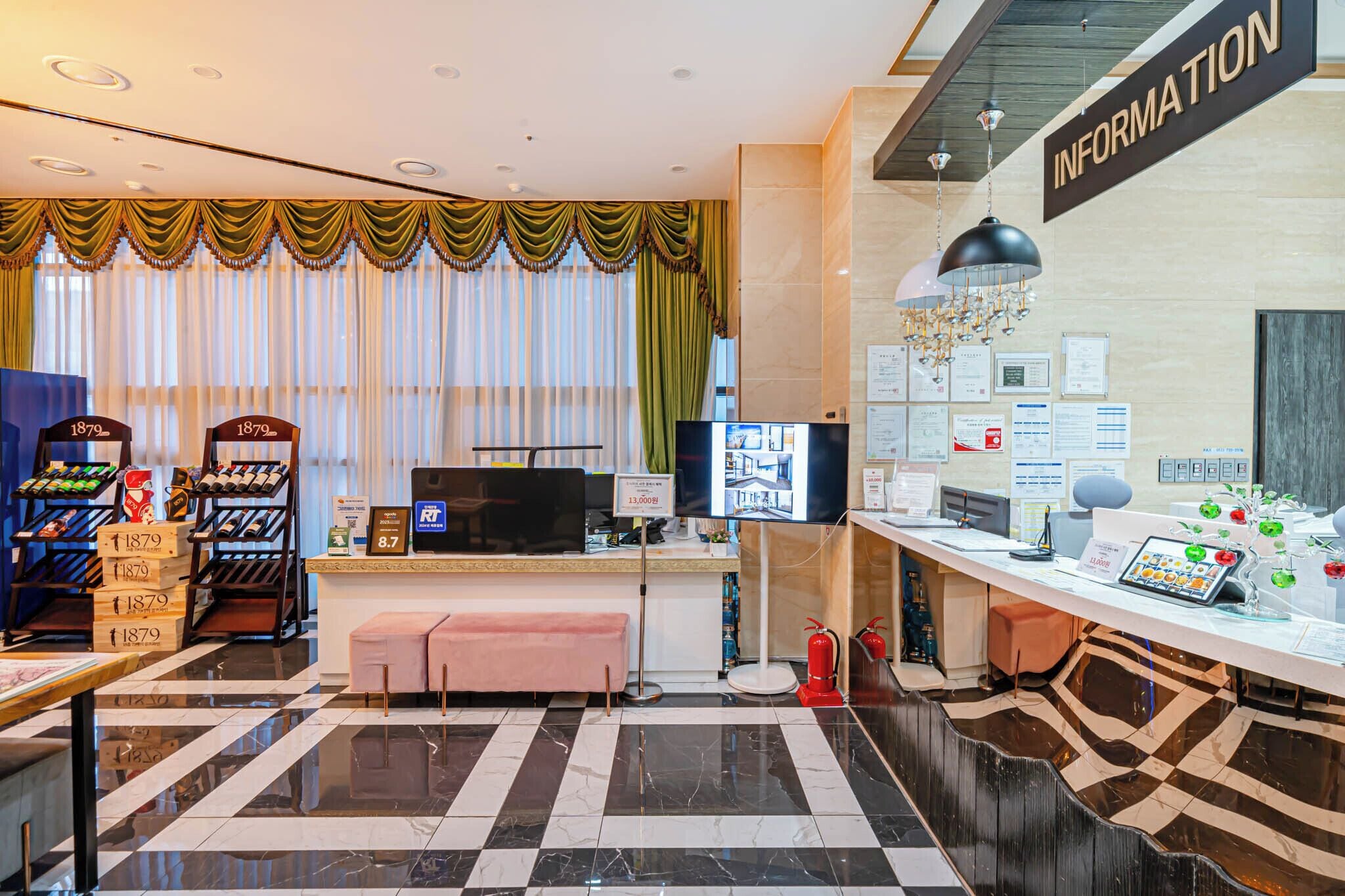 A hotel reception area with a check-in counter, a television, and a wall displaying various informational posters.