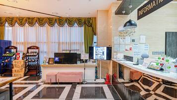 A hotel reception area with a check-in counter, a television, and a wall displaying various informational posters.