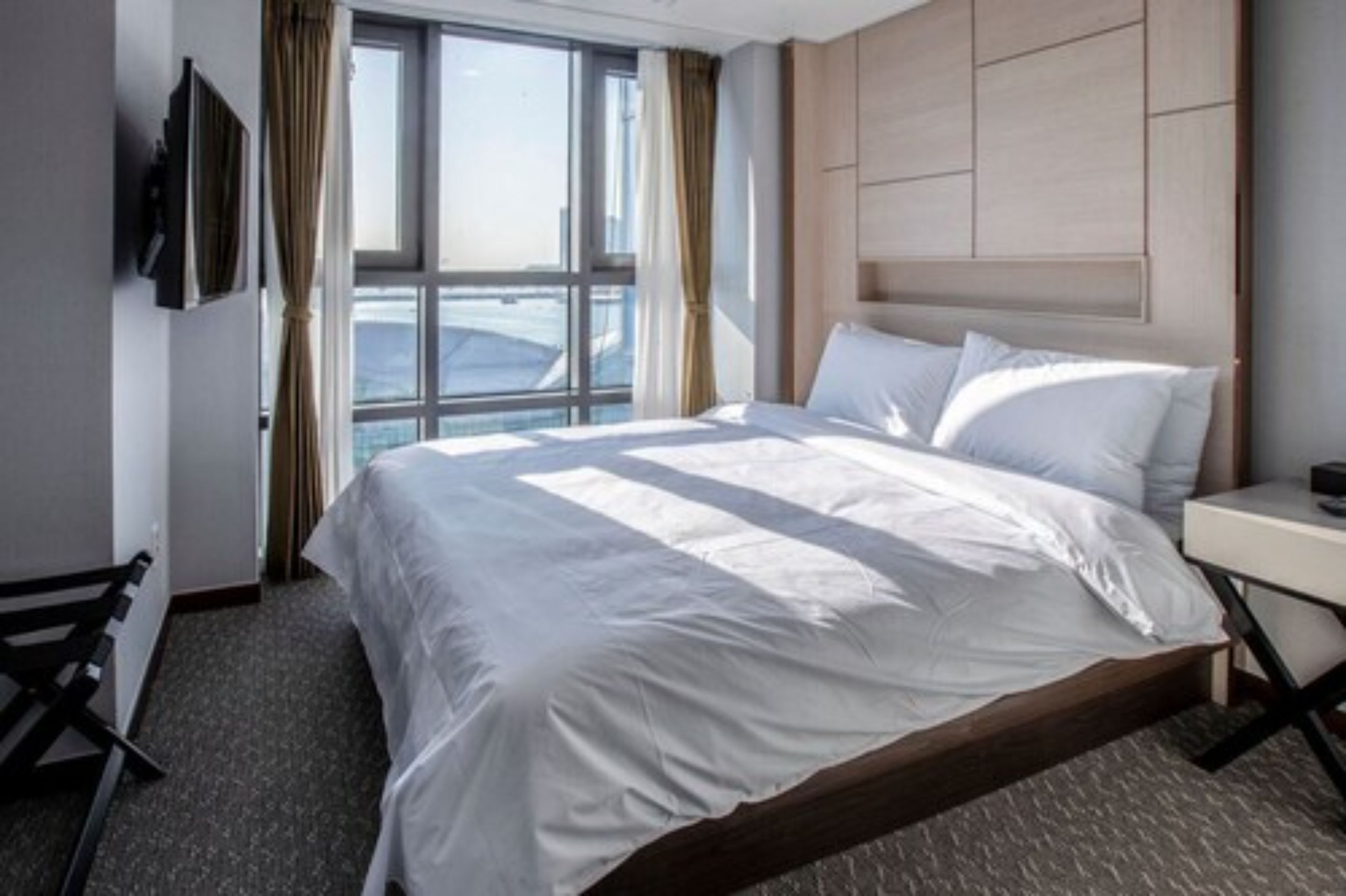 Een moderne hotelkamer met een groot bed, nachtkastje, tv aan de muur en raam met gordijnen.