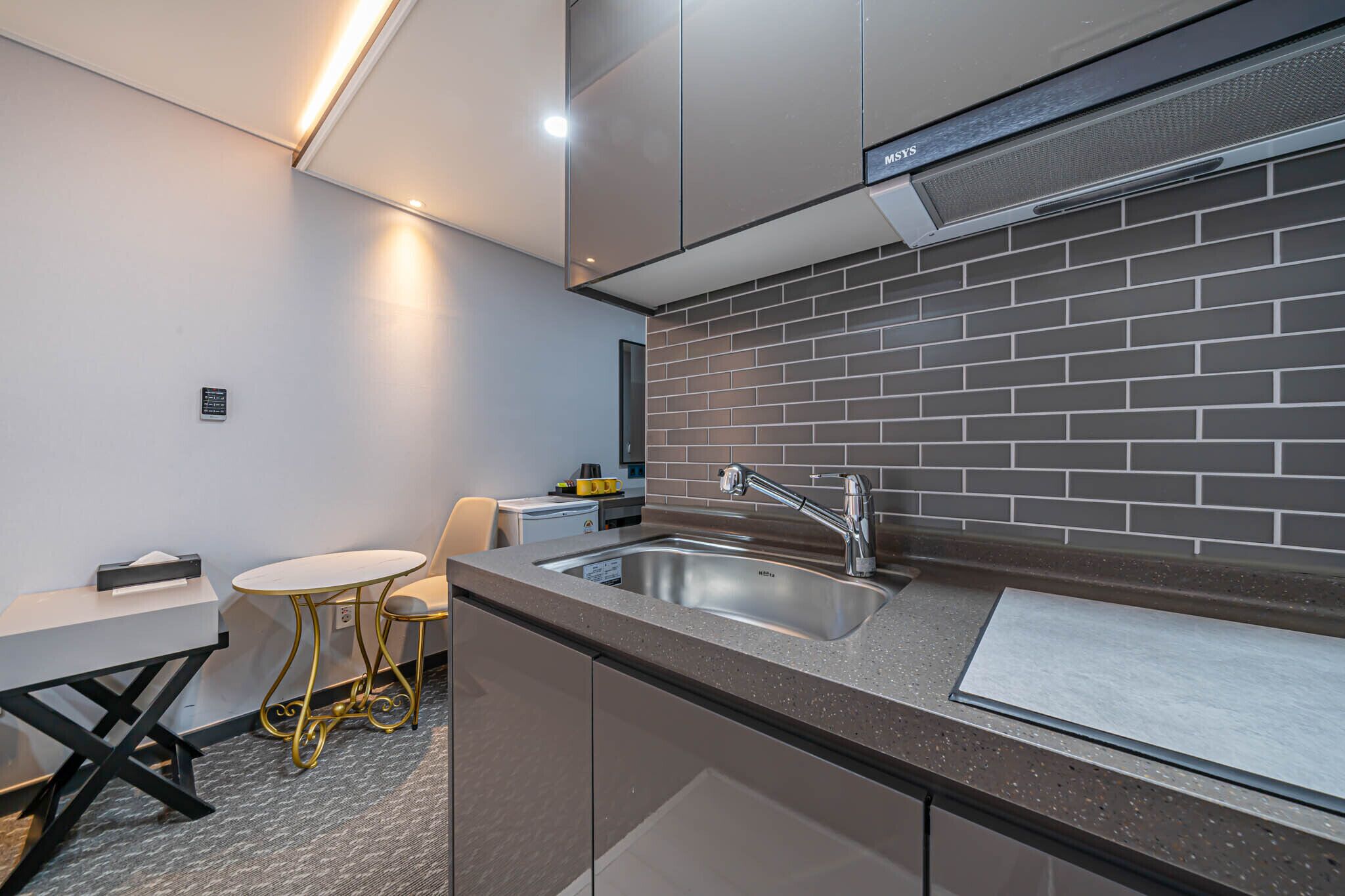 Ett kompakt kök med modern design, utrustat med en diskho i rostfritt stål, ett litet runt bord och en praktisk bänkskiva.