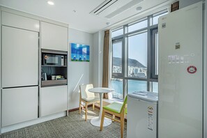 A modern hotel room with a kitchenette, a dining area with a table and chairs, and a large window offering a city view. - Griffin Bay Hotel (Busan)