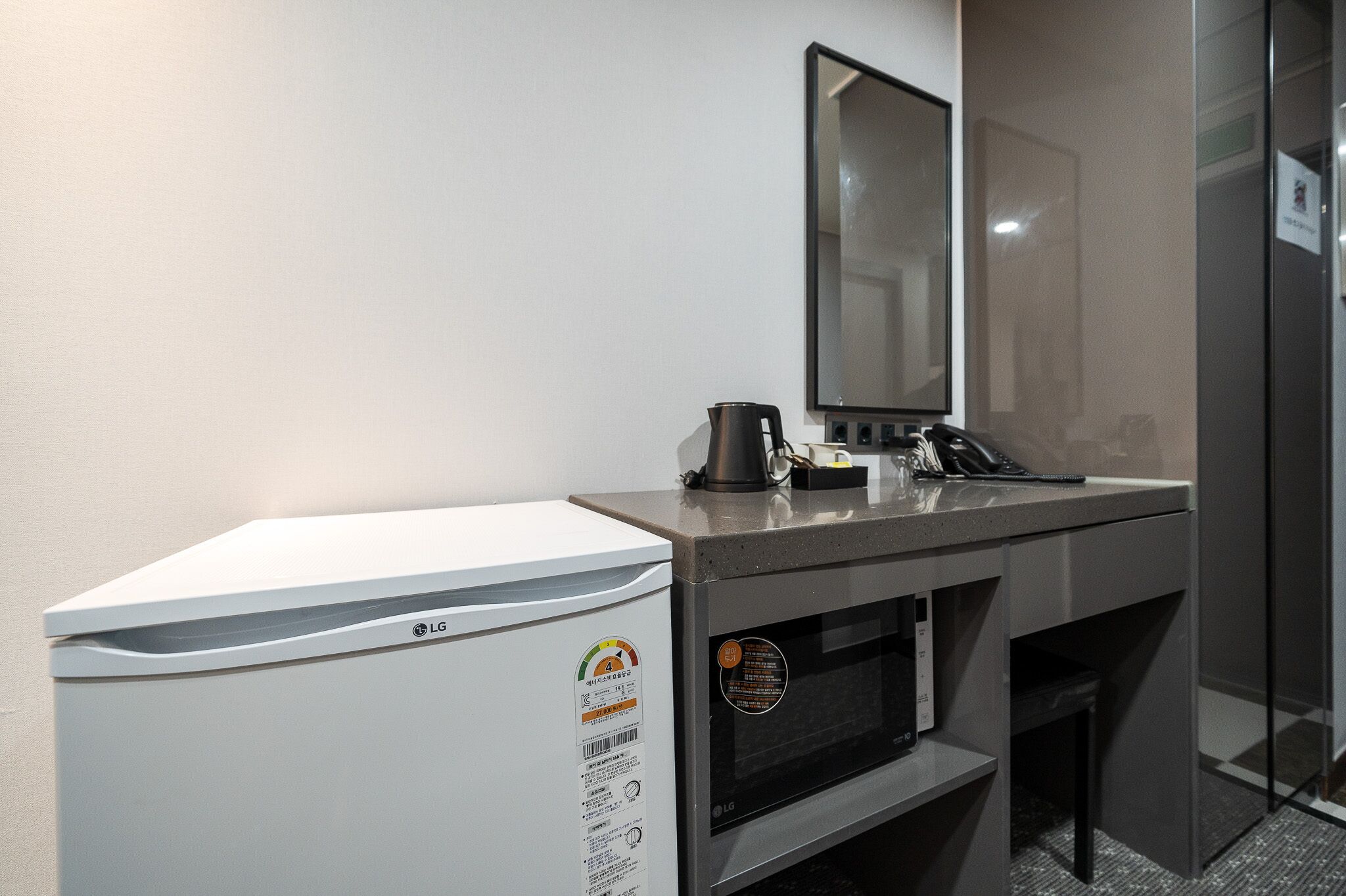 Ein kleines Badezimmer mit einem weißen LG-Kühlschrank, einem Waschbecken mit Spiegel und einer Kaffeemaschine.