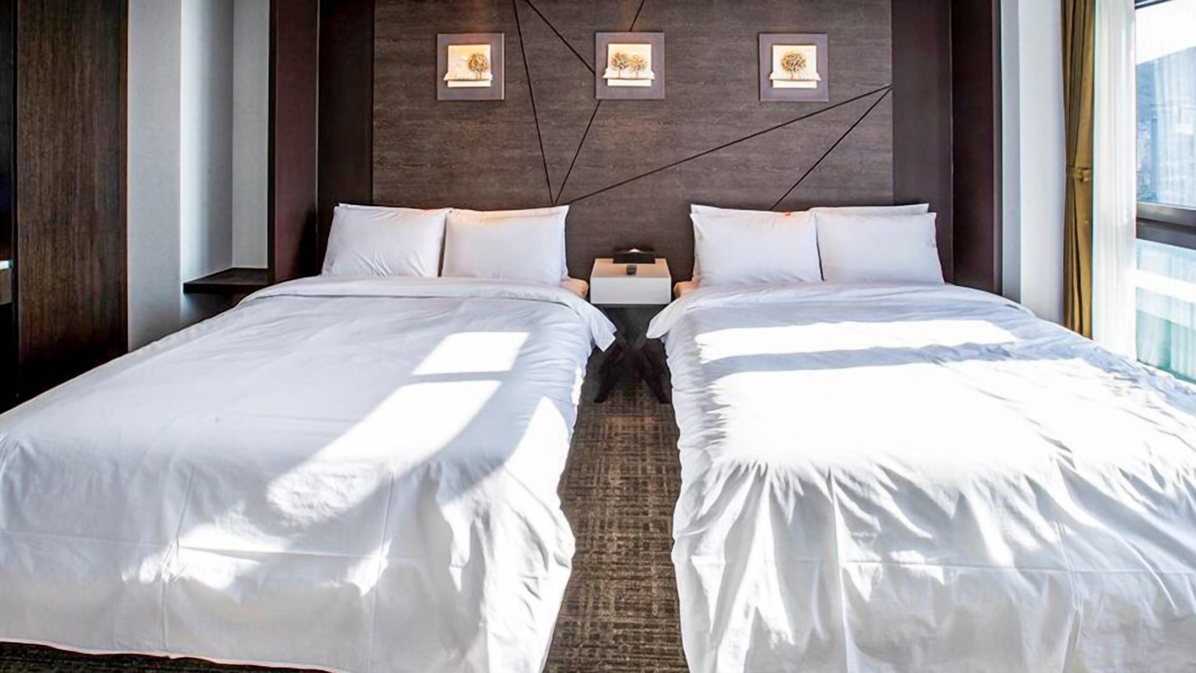A hotel room with two beds, a dark wooden headboard, and framed artwork on the wall.