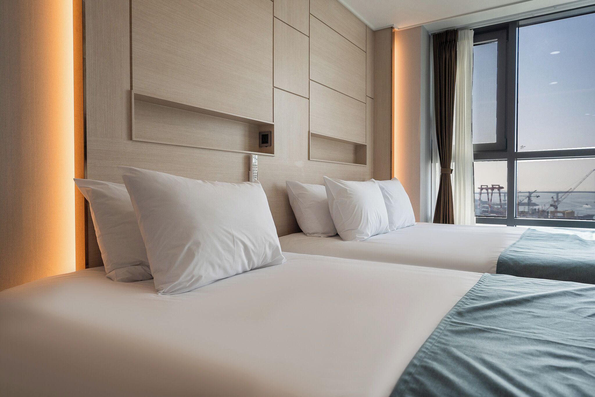 A hotel room with two beds, a large window with a view of the city, and a modern headboard.