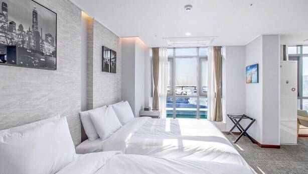 A hotel room with a large bed, a view of the city skyline, and a balcony with a pool. - Griffin Bay Hotel (Busan)