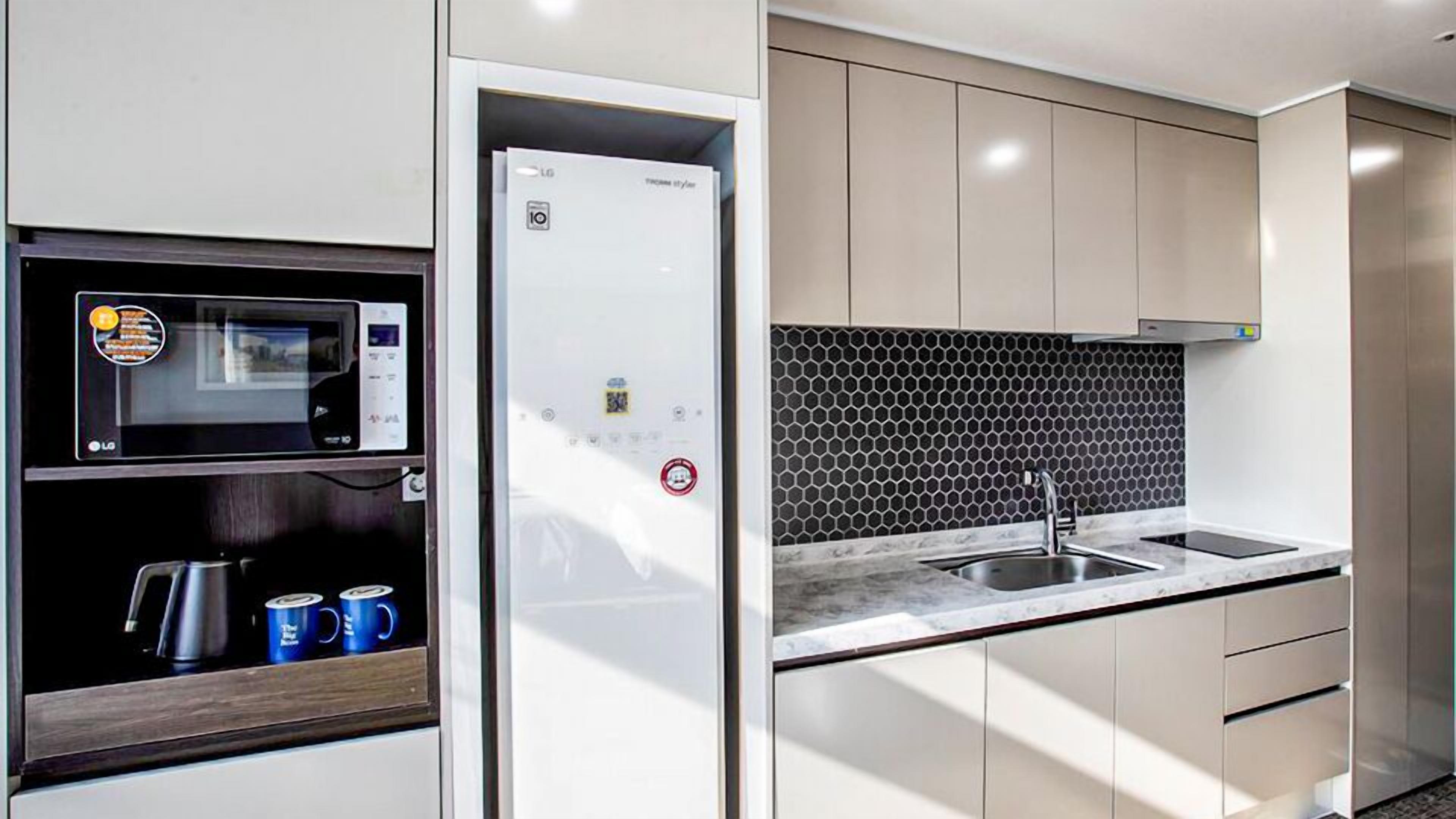 Een moderne keuken met een magnetron, koelkast, spoelbak en kastjes.