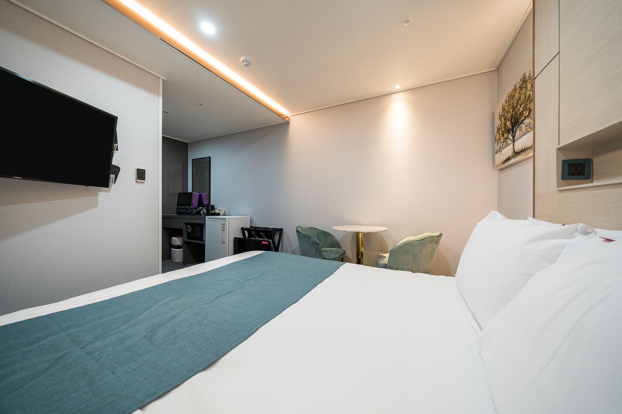 A hotel room with a bed, a desk, a chair, a TV, and a lamp.