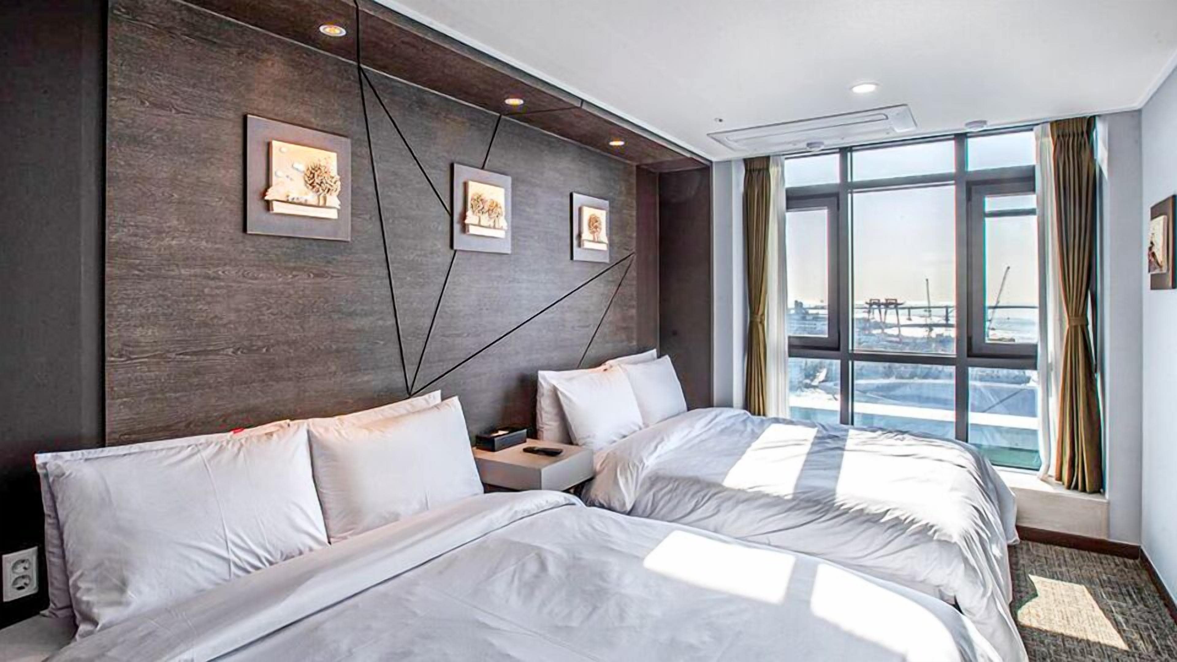 A hotel room with two beds, a large window with a view, and artwork on the wall.