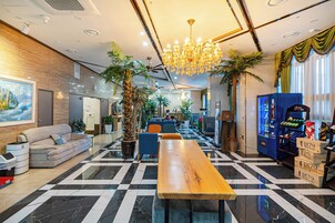 A hotel lobby with a checkered floor, a wooden reception desk, a chandelier, and a vending machine.