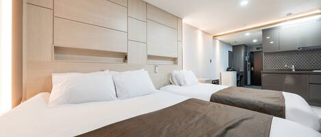 A hotel room with two beds, a wooden headboard, a kitchenette, and a bathroom.