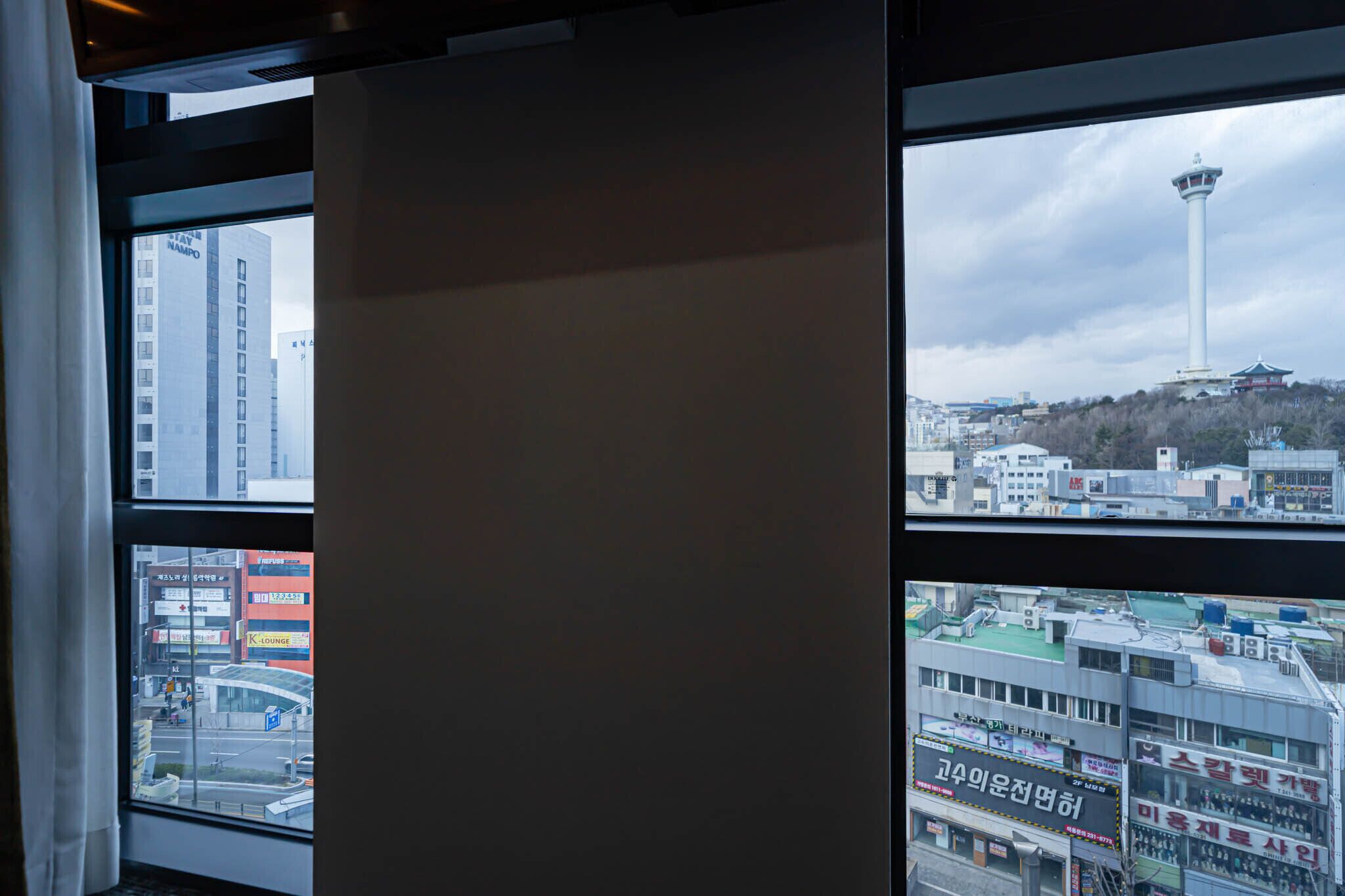 A view through a window with a cityscape, including a tower and various buildings.