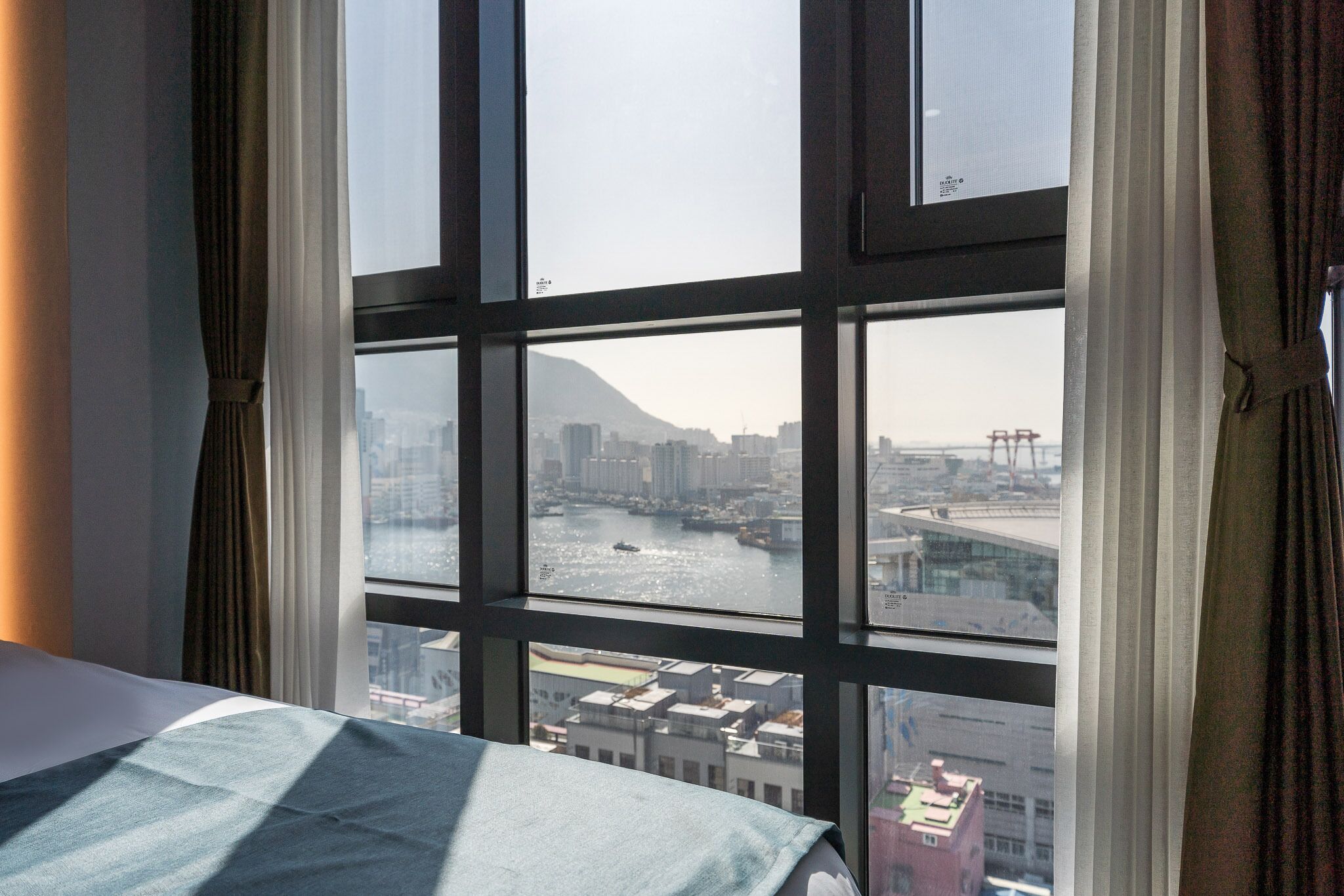 A hotel room with a large window offering a view of a cityscape, including a river and buildings.