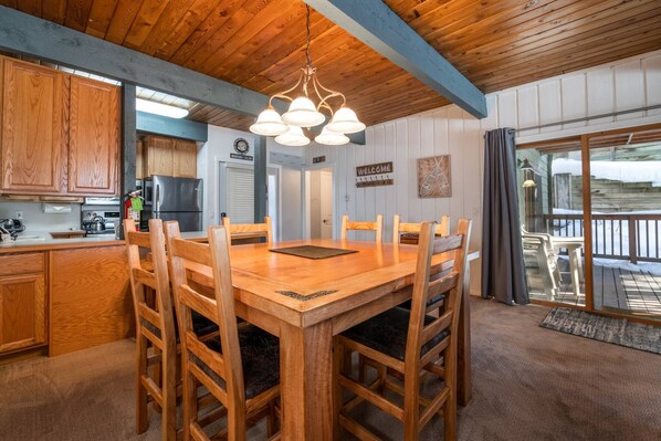 A wooden dining table with six chairs, a kitchen with wooden cabinets, a refrigerator, and a hanging light fixture. - Walk 240 yds to Resort+Steps to Hot Tub/Free Town/Ski Bus-Wood Stove/Cabin Like Setting-Covered Deck (Steamboat Springs)