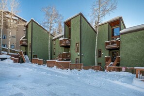 A row of green brick buildings with wooden balconies and a snow-covered ground.