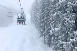 A ski lift with passengers ascending a snowy slope, surrounded by snow-covered trees.