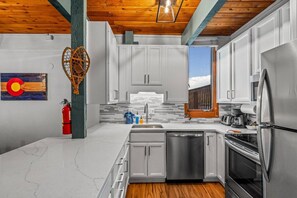 A modern kitchen with white cabinets, stainless steel appliances, and a wooden ceiling.