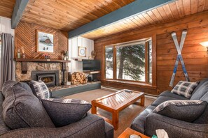 A cozy cabin interior with a stone fireplace, wooden walls, a large window with a view of trees, and a ski rack. - Walk 240 yds to Resort+Steps to Hot Tub/Free Town/Ski Bus-Wood Stove/Cabin Like Setting-Covered Deck (Steamboat Springs)