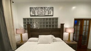 A bedroom with a large bed, two bedside lamps, a window with a view of a building, and a door. - Stylish one bedroom apartment in downtown Jackson (Jackson)