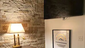 A room with a stone wall, a desk with a lamp, a framed picture, and a flat-screen TV mounted on the wall. - Stylish one bedroom apartment in downtown Jackson (Jackson)