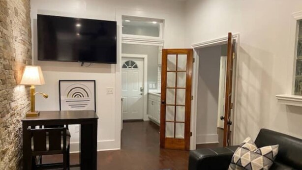 A living room with a black leather sofa, a small table with a lamp, and a TV mounted on the wall. - Stylish one bedroom apartment in downtown Jackson (Jackson)
